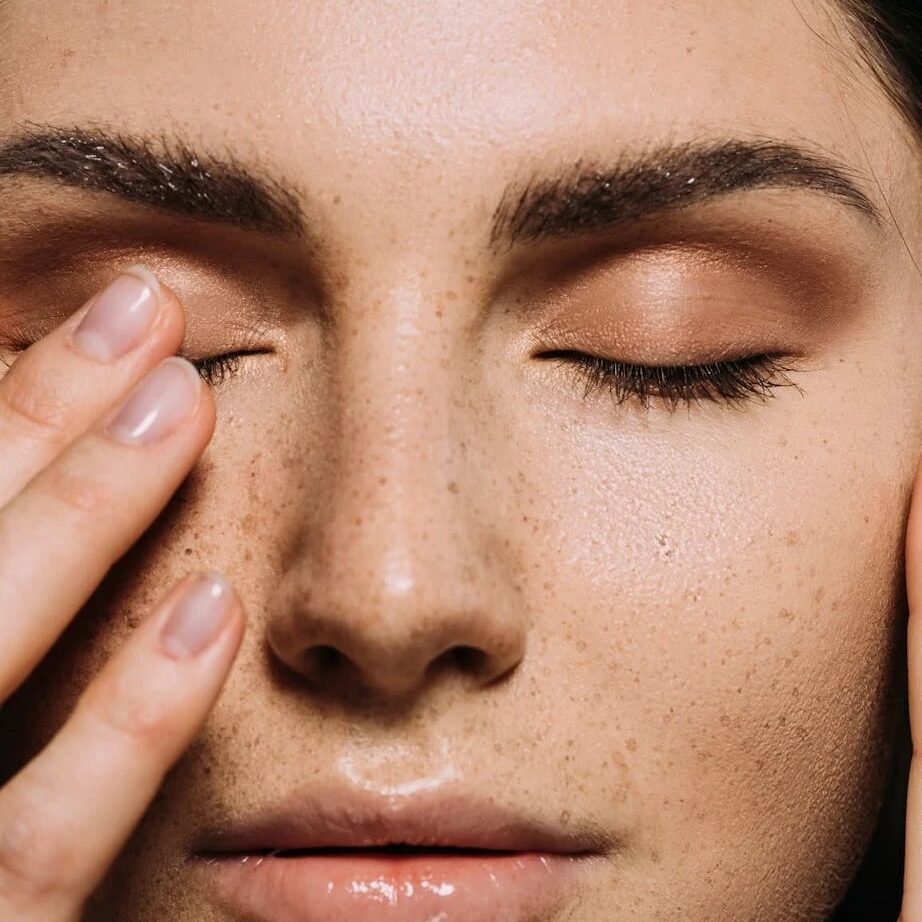 A woman with her eyes closed touching the side of her face.