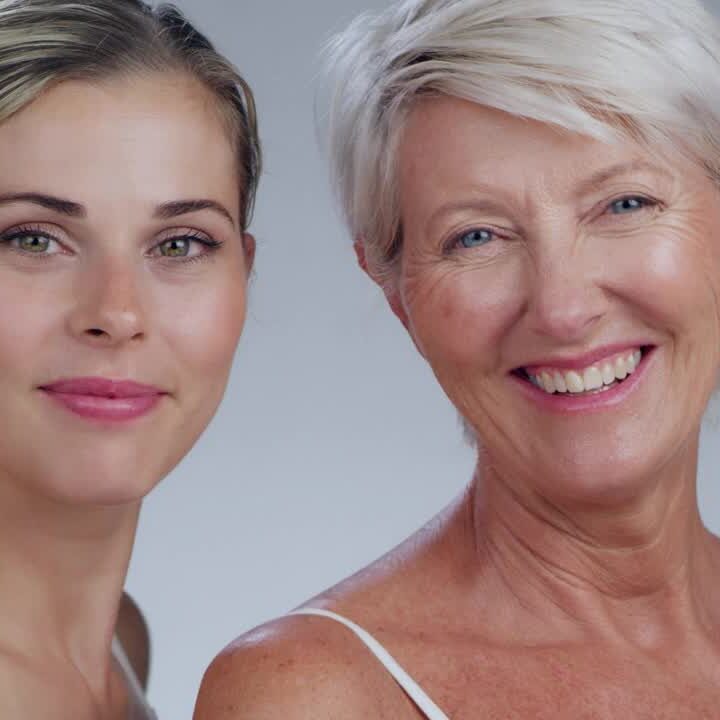 Two women posing for a picture in front of a white wall.